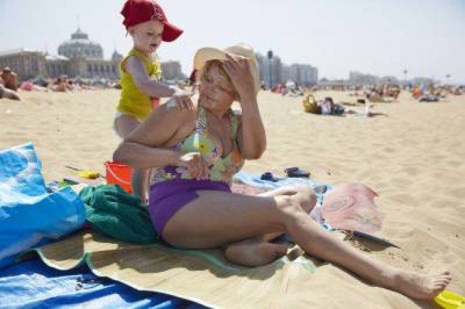 A grandchild protects his grandmother with sunscreen on a sunny day at the Scheveningen beach on July 18, 2013. AFP PHOTO / ANP - MARTIJN BEEKMAN netherlands out