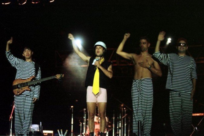 Os integrantes do grupo Mamonas Assassinas, Bento (e), Dinho(c), Samuel Reoli (sem camisa) e Julio Rasec (óculos) durante último Show, no Estádio Mané Garrincha, nos anos 1990. - (foto: Tina Coelho/CB/D.A Press) Os integrantes do grupo Mamonas Assassinas, Bento (e), Dinho(c), Samuel Reoli (sem camisa) e Julio Rasec (óculos) durante último Show, no Estádio Mané Garrincha, nos anos 1990. - (foto: Tina Coelho/CB/D.A Press)