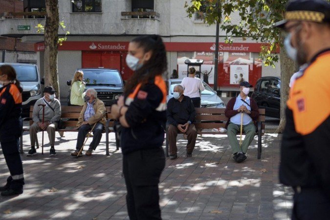 Alguns vizinhos sentam-se em um banco enquanto membros da Defesa Civil informam aos moradores sobre as novas restrições impostas ao bairro sob o bloqueio parcial de Usera, em Madrid, Espanha. - (crédito: OSCAR DEL POZO / AFP) Alguns vizinhos sentam-se em um banco enquanto membros da Defesa Civil informam aos moradores sobre as novas restrições impostas ao bairro sob o bloqueio parcial de Usera, em Madrid, Espanha. - (crédito: OSCAR DEL POZO / AFP)