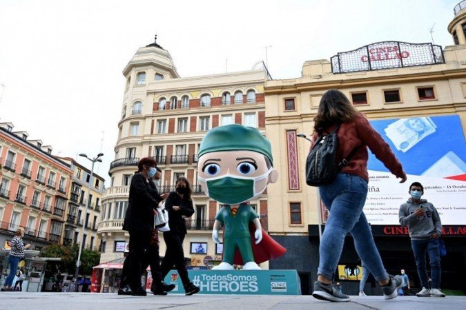 Pessoas usando máscaras caminham ao lado de uma estátua de 6 metros de altura, respeitando um Pessoas usando máscaras caminham ao lado de uma estátua de 6 metros de altura, respeitando um