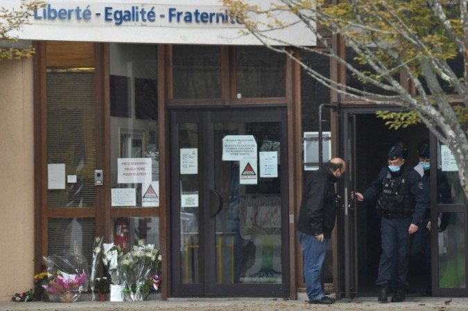 A polícia francesa CRS (Compagnies Republicaines de Securite) na porta de uma escola secundária em Conflans-Sainte-Honorine, 30 km a noroeste de Paris, em 17 de outubro de 2020, ao lado de flores expostas depois que um professor foi decapitado por um agressor que foi morto a tiros por policiais. - (crédito: Bertrand GUAY / AFP) A polícia francesa CRS (Compagnies Republicaines de Securite) na porta de uma escola secundária em Conflans-Sainte-Honorine, 30 km a noroeste de Paris, em 17 de outubro de 2020, ao lado de flores expostas depois que um professor foi decapitado por um agressor que foi morto a tiros por policiais. - (crédito: Bertrand GUAY / AFP)