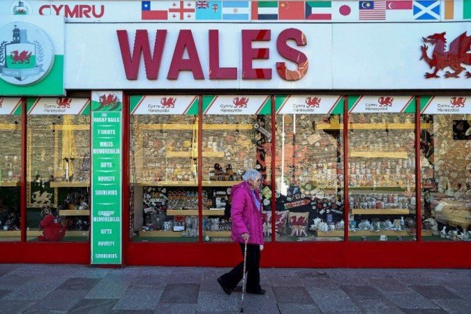 Nesta foto de arquivo tirada em 27 de setembro de 2020, uma mulher usando uma viseira protetora passa por uma loja de souvenirs que vende itens com o tema galês, em Cardiff, no sul do País de Gales. - (crédito: Geoff Caddick / AFP) Nesta foto de arquivo tirada em 27 de setembro de 2020, uma mulher usando uma viseira protetora passa por uma loja de souvenirs que vende itens com o tema galês, em Cardiff, no sul do País de Gales. - (crédito: Geoff Caddick / AFP)