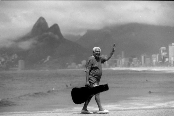 Fotografia do músico Dorival Caymmi, com case de violão, caminhando na orla da praia - (crédito: Arquivo Pessoal) Fotografia do músico Dorival Caymmi, com case de violão, caminhando na orla da praia - (crédito: Arquivo Pessoal)