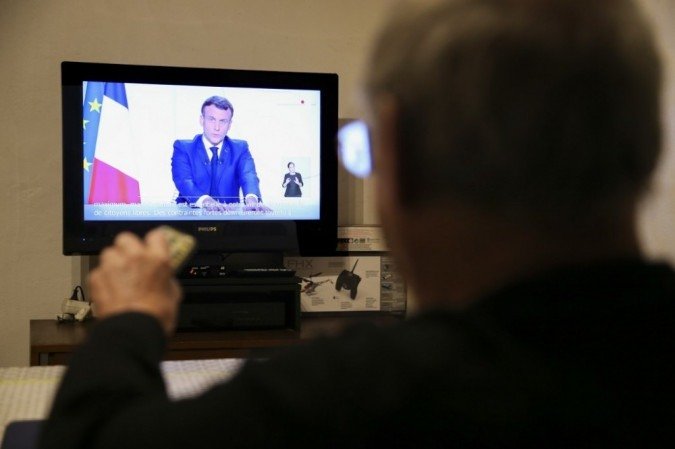 Um homem assiste ao presidente francês Emmanuel Macron na televisão, em 24 de novembro de 2020, enquanto o presidente francês fala durante um discurso televisionado para a Nação sobre a pandemia Covid-19 e medidas de bloqueio na França. - (crédito: Pascal POCHARD-CASABIANCA / AFP) Um homem assiste ao presidente francês Emmanuel Macron na televisão, em 24 de novembro de 2020, enquanto o presidente francês fala durante um discurso televisionado para a Nação sobre a pandemia Covid-19 e medidas de bloqueio na França. - (crédito: Pascal POCHARD-CASABIANCA / AFP)