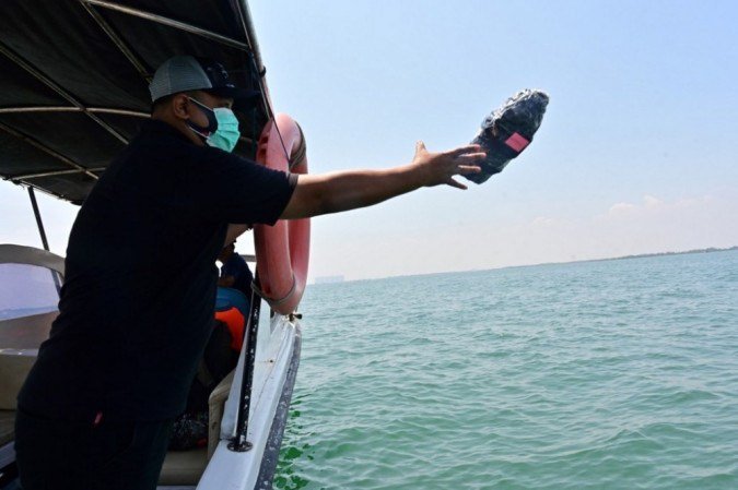 Esta foto tirada em 20 de outubro de 2020 mostra Eric Ragaputra, um técnico da empresa CLS Argos, jogando um dispositivo de monitoramento de plástico com balizas de satélite no mar para monitorar os resíduos na costa de Teluk Naga, Tangerang, província de Banten. 