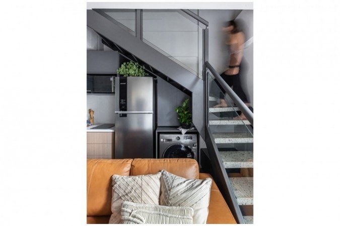 O projeto aproveitou o espaço embaixo da escada para acomodar a geladeira e a máquina de lavar e secar roupas