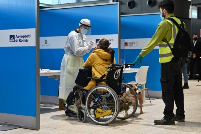 Um passageiro deficiente (C) que acabou de pousar de Nova York em um voo da Alitalia passa por um teste rápido de antígeno para covid-19 em 9 de dezembro de 2020 em uma estação de testes montada no aeroporto Fiumicino de Roma. -  (crédito: ANDREAS SOLARO / AFP)