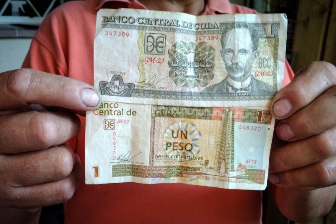 Um trabalhador cubano mostra 1 CUP (pesos cubanos - parte superior) e 1 CUC (pesos cubanos conversíveis - parte inferior) em Havana.  -  (crédito: Adalberto ROQUE / AFP)