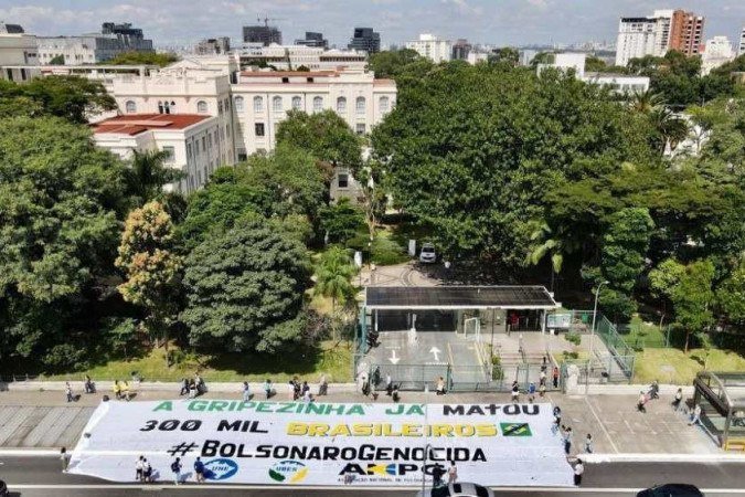 Vista aérea de uma manifestação. Abaixou a um cartaz branco com os dizeres "A gripezinha já matou mais de 300 mil brasileiros. #BolsonaroGenocida". Acima, há uma rua de asfalto e várias árvores com um prédio ao fundo. - (crédito: Divulgação / UNE) Vista aérea de uma manifestação. Abaixou a um cartaz branco com os dizeres "A gripezinha já matou mais de 300 mil brasileiros. #BolsonaroGenocida". Acima, há uma rua de asfalto e várias árvores com um prédio ao fundo. - (crédito: Divulgação / UNE)