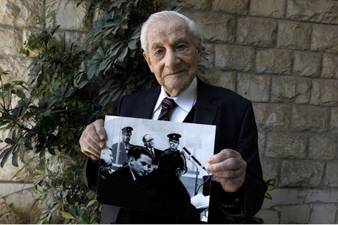 Gabriel Bach, 93, ex-juiz da Suprema Corte de Israel e ex-procurador adjunto durante o julgamento do importante oficial nazista alemão Adolf Eichmann, posa para uma foto enquanto segura uma foto que o mostra (abaixo) durante o de Eichmann (topo ) julgamento, no quintal de sua casa em Jerusalém em 3 de maio de 2020. Dias depois de Israel anunciar que Eichmann havia sido preso e trazido ao país para julgamento, Bach - então servindo como procurador do estado - recebeu uma atribuição que alterou permanentemente sua vida. Bach era o procurador-geral adjunto de Israel quando, há 60 anos neste mês, o mundo soube que um dos principais arquitetos da 