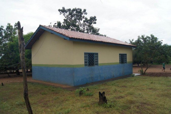 A escola está cercada por árvores. É uma construção com duas janelas e está pintada de amarelo com azul e uma listra verde entre as cores. A escola está cercada por árvores. É uma construção com duas janelas e está pintada de amarelo com azul e uma listra verde entre as cores.