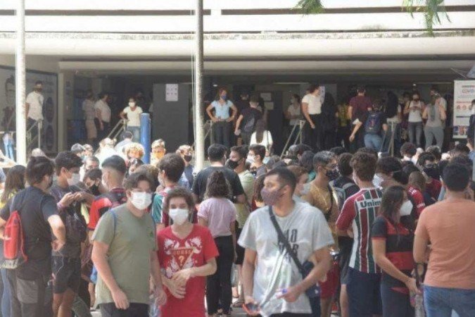 Estudantes em frente à uma escola usando máscara.