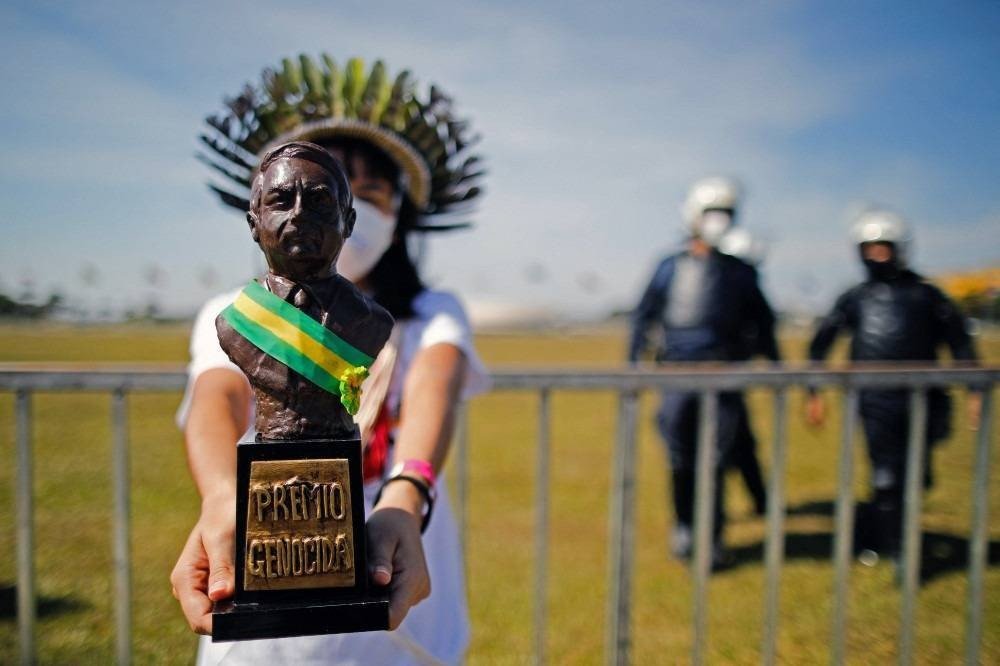 Um ativista indígena entrega um 'prêmio genocida' ao presidente Jair Bolsonaro durante um protesto de partidos de oposição e movimentos sociais contra o tratamento da pandemia COVID-19 em Brasília, em 19 de junho de 2021. O presidente de extrema direita Jair Bolsonaro vem enfrentando críticas por sua gestão da pandemia, incluindo inicialmente recusar ofertas de vacinas, como os epidemiologistas alertam que o Brasil pode agora estar à beira de uma terceira onda de Covid-19.