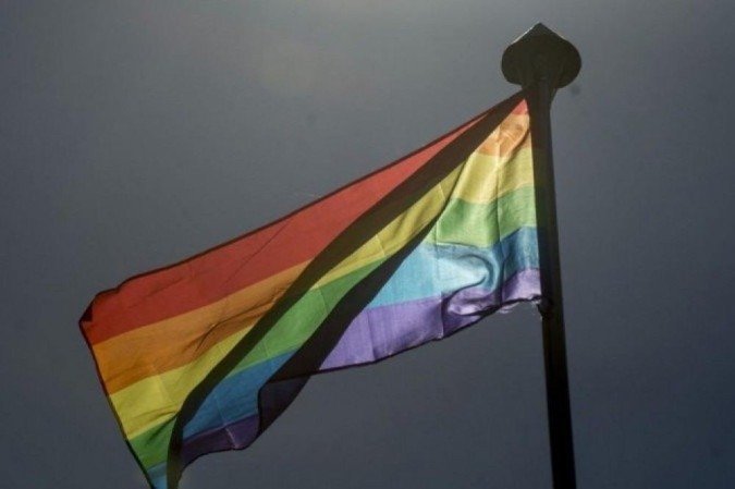 Bandeira com as cores que representam as cores da comunidade LGBTQIA+ hasteada em um mastro. No fundo da foto, um céu cinzento - (crédito: Marcelo Camargo/Agência Brasil) Bandeira com as cores que representam as cores da comunidade LGBTQIA+ hasteada em um mastro. No fundo da foto, um céu cinzento - (crédito: Marcelo Camargo/Agência Brasil)