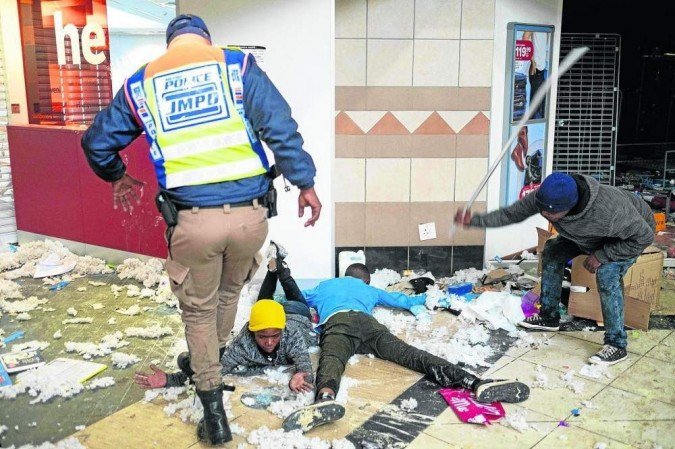Polícia de Johannesburgo pisa sobre o braço de suposto vândalo, enquanto outro homem o agride com barra de ferro: revolta afeta duas províncias -  (crédito: Emmanuel Croset/AFP)