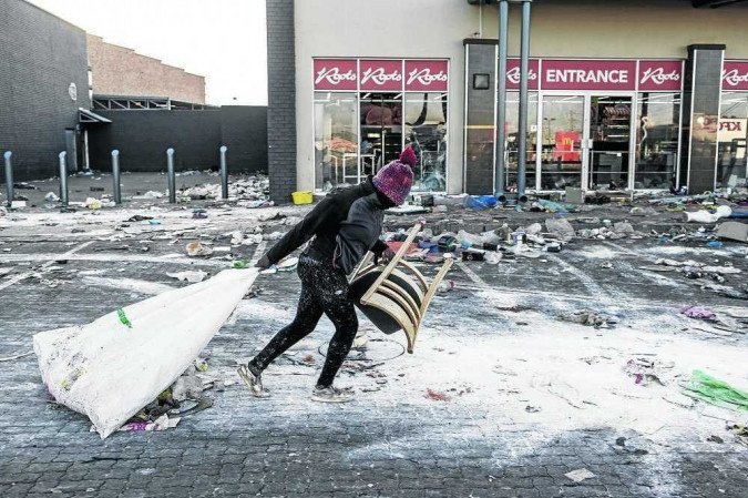 Saqueador carrega cadeira e objetos dentro de saco, roubados de uma loja em Vosloorus, na periferia de Johannesburgo - (crédito: Marco Longari/AFP) Saqueador carrega cadeira e objetos dentro de saco, roubados de uma loja em Vosloorus, na periferia de Johannesburgo - (crédito: Marco Longari/AFP)