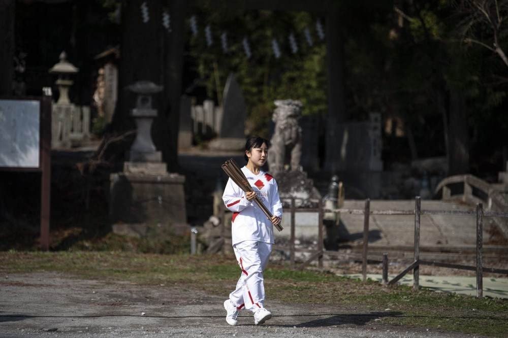 O portador da tocha Rio Suzuki, um estudante do ensino médio, chega com a tocha olímpica apagada antes do início do segundo dia do revezamento da tocha dos Jogos Olímpicos de Tóquio 2020 no Santuário Somanakamura na cidade de Soma, província de Fukushima em março