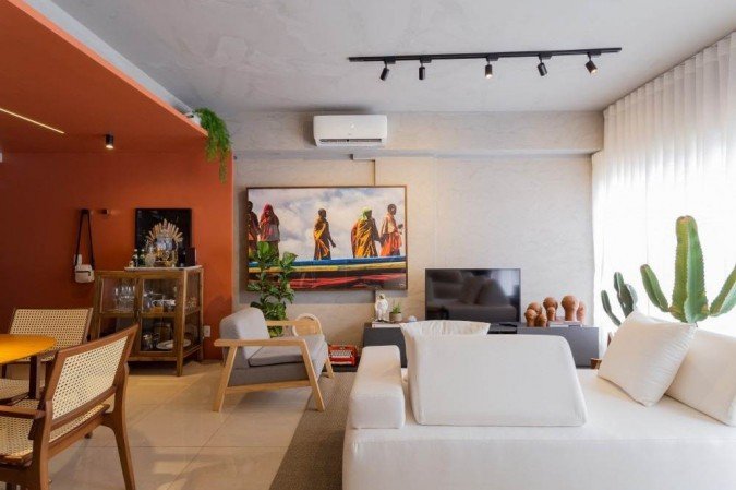 Apesar da unidade entre sala e quarto, o sofá-cama e a iluminação no teto promovem uma divisão. Enquanto a decoração do quarto é neutra, a sala traz cor e objetos de arte, que deixam o espaço convidativo