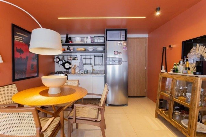 

Neste espaço, diferenciado pelas paredes laranja, que criam uma divisão de ambiente, fica a cozinha e uma espécie de sala de jantar. O espaço é bem aproveitado e os utensílios ficam expostos