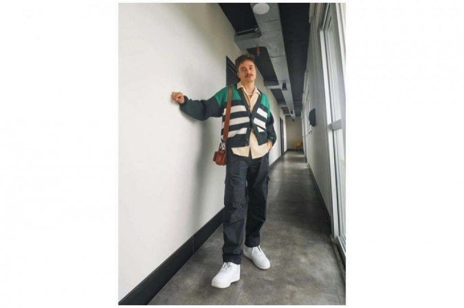 O duo camisa + cardigan sai do convencional com a calça de caimento mais largo e os sneakers brancos na composição usada pelo influenciador Caio Bigodi
