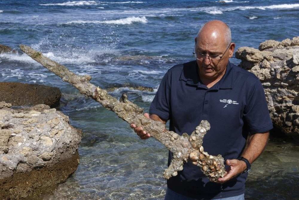 Jacob Sharvit of the Israel Antiquities Authority displays an ancient one-meter-long sword that experts say dates back to the Crusader-era and is believed to have belonged to a Crusader, displayed at the beach in the Israeli seaport of Caesarea, on October 19, 2021 some days after being discovered by a local diver. (Photo by JACK GUEZ / AFP)