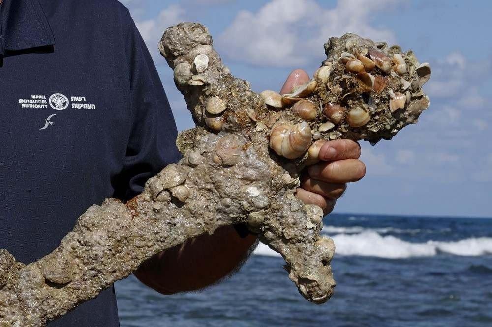 Jacob Sharvit of the Israel Antiquities Authority displays an ancient one-meter-long sword that experts say dates back to the Crusader-era and is believed to have belonged to a Crusader, displayed at the beach in the Israeli seaport of Caesarea, on October 19, 2021 some days after being discovered by a local diver. (Photo by JACK GUEZ / AFP)