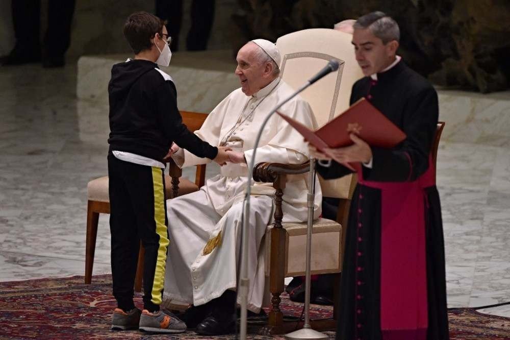 Pope Francis (C) is greeted by a child during the weekly general audience at Paul-VI hall in the Vatican on October 20, 2021. (Photo by ANDREAS SOLARO / AFP)
      Caption