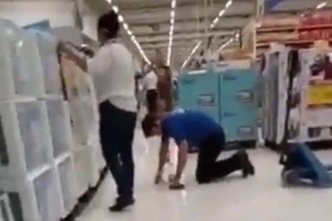 Pelo vídeo é possível observar uma mulher em pé ao lado do homem de joelhos. Ela parece registrar o momento com um celular -  (crédito: Reprodução/Twitter)