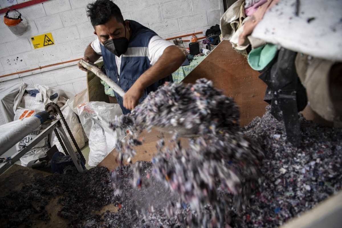  A man works at a factory that recycles used clothes discarded in the Atacama desert for wooden isolation panels for the walls of social housing, in Alto Hospicio, Iquique, Chile, on September 27, 2021. - EcoFibra, Ecocitex and Sembra are circular economy projects that have textile waste as their raw material. The textile industry in Chile will be included in the law of Extended Responsibility of the Producer (REP), forcing clothes and textiles importers take charge of the waste they generate. (Photo by MARTIN BERNETTI / AFP)
      Caption 