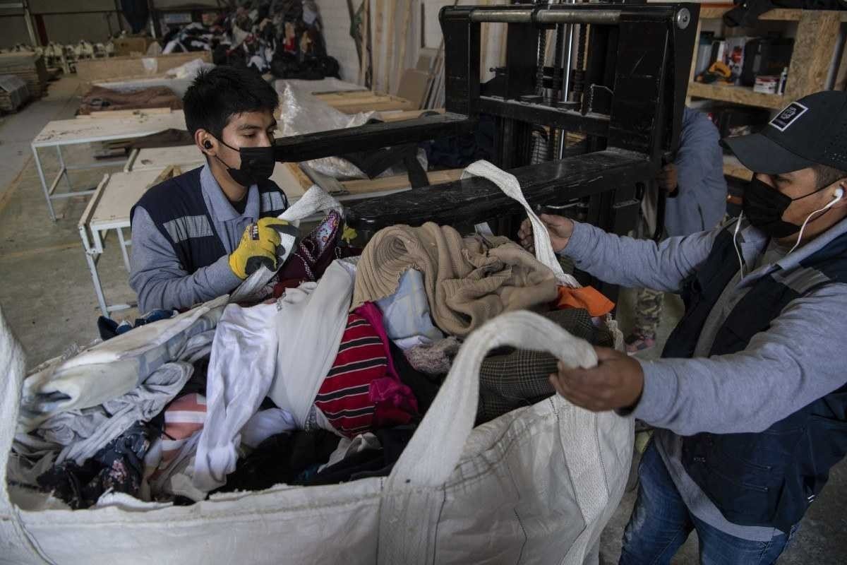  Men work at a factory that recycles used clothes discarded in the Atacama desert for wooden isolation panels for the walls of social housing, in Alto Hospicio, Iquique, Chile, on September 27, 2021. - EcoFibra, Ecocitex and Sembra are circular economy projects that have textile waste as their raw material. The textile industry in Chile will be included in the law of Extended Responsibility of the Producer (REP), forcing clothes and textiles importers take charge of the waste they generate. (Photo by MARTIN BERNETTI / AFP)
      Caption 