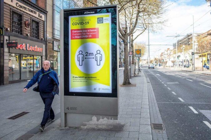 Pedestre passa diante de pôster alertando para a importância do distanciamento social, em Dublin, na Irlanda