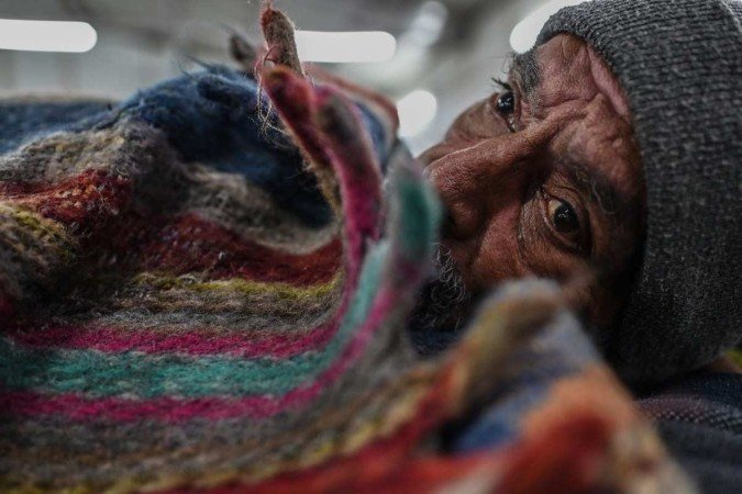 Nesta foto tirada em 29 de janeiro de 2022, mostra um sem-teto envolto em uma colcha sentado dentro de um abrigo istrado pelo governo em Nova Délhi. - (crédito: SAJJAD HUSSAIN / AFP) Nesta foto tirada em 29 de janeiro de 2022, mostra um sem-teto envolto em uma colcha sentado dentro de um abrigo istrado pelo governo em Nova Délhi. - (crédito: SAJJAD HUSSAIN / AFP)