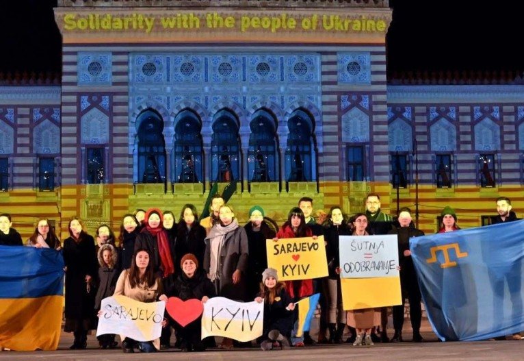 Um pequeno grupo de cidadãos se reúne em frente à prefeitura de Sarajevo iluminada com as cores da bandeira ucraniana, no final de 24 de fevereiro de 2022. - A agência de refugiados da ONU disse que cerca de 100.000 pessoas fugiram de suas casas na Ucrânia e vários milhares mais haviam deixou o país desde que a vizinha Rússia invadiu no início de 24 de fevereiro. 'Acreditamos que cerca de 100.000 pessoas já devem ter deixado suas casas e podem estar deslocadas dentro do país, e vários milhares cruzaram fronteiras internacionais', disse a porta-voz do ACNUR Shabia Mantoo à AFP.      Caption 