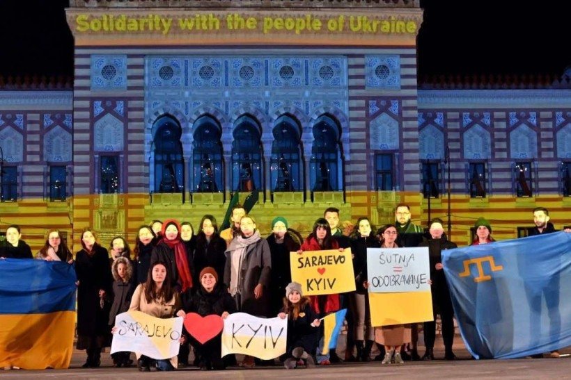 Um pequeno grupo de cidadãos se reúne em frente à prefeitura de Sarajevo iluminada com as cores da bandeira ucraniana, no final de 24 de fevereiro de 2022. - A agência de refugiados da ONU disse que cerca de 100.000 pessoas fugiram de suas casas na Ucrânia e vários milhares mais haviam deixou o país desde que a vizinha Rússia invadiu no início de 24 de fevereiro. 'Acreditamos que cerca de 100.000 pessoas já devem ter deixado suas casas e podem estar deslocadas dentro do país, e vários milhares cruzaram fronteiras internacionais', disse a porta-voz do ACNUR Shabia Mantoo à AFP.      Caption 