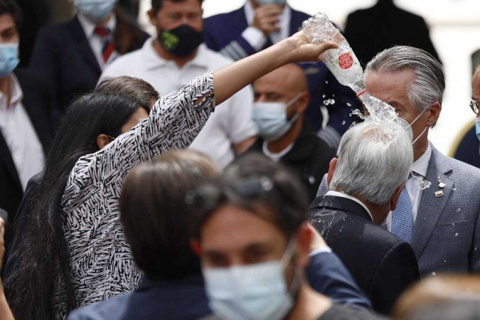 Nesta foto divulgada pela ATON, uma mulher não identificada joga água para o presidente Sebastian Pinera (R) durante um evento relacionado à pandemia de Covid-19 no Palácio Presidencial La Moneda, em Santiago, em 3 de março de 2022. Caption - (crédito: Dragomir YANKOVIC / ATON CHILE / AFP) Nesta foto divulgada pela ATON, uma mulher não identificada joga água para o presidente Sebastian Pinera (R) durante um evento relacionado à pandemia de Covid-19 no Palácio Presidencial La Moneda, em Santiago, em 3 de março de 2022. Caption - (crédito: Dragomir YANKOVIC / ATON CHILE / AFP)