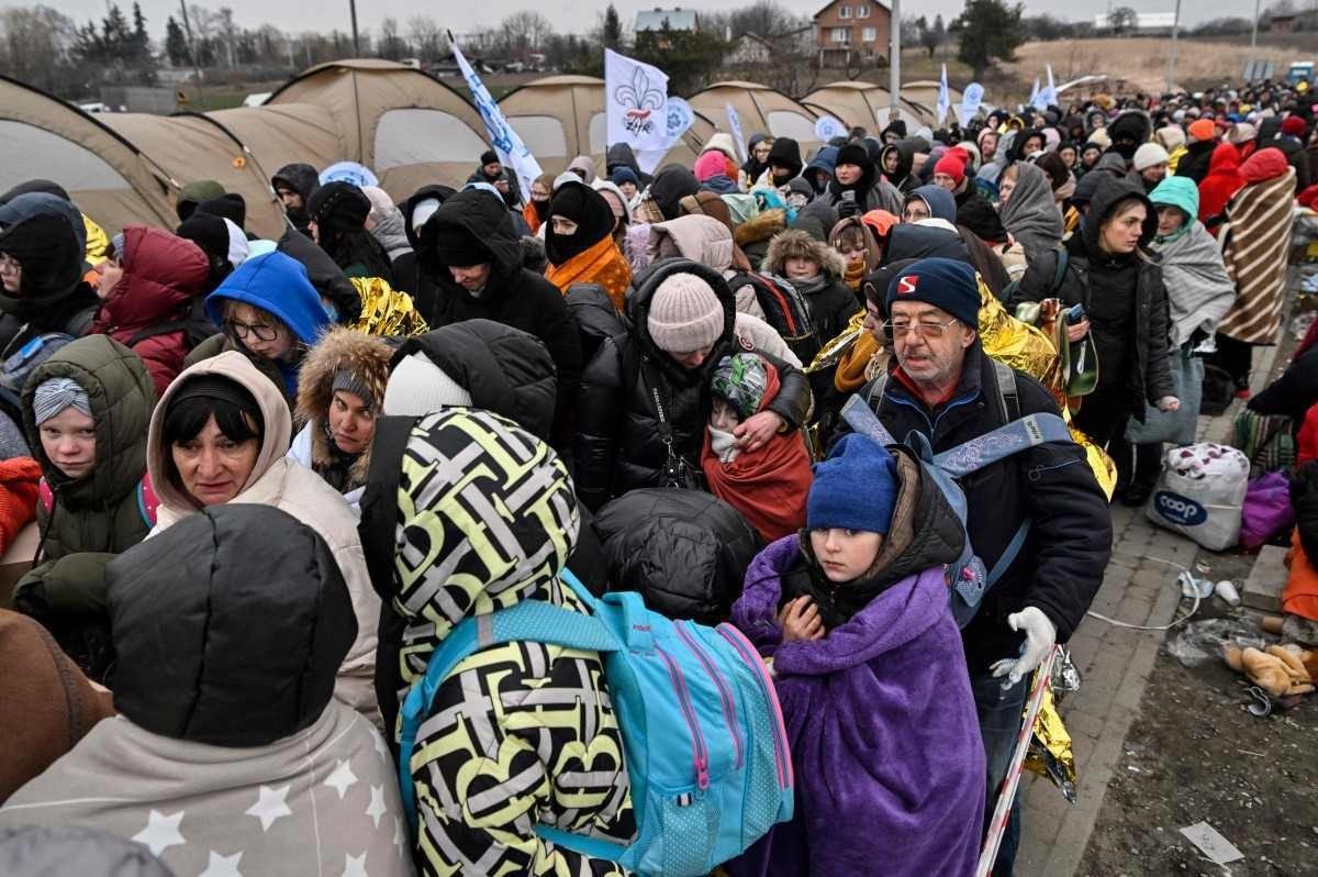  TOPSHOT - Refugees stand in line in the cold as they wait to be transferred to a train station after crossing the Ukrainian border into Poland, at the Medyka border crossing in Poland, on March 7, 2022.   More than 1.5 million people have fled Ukraine since the start of the Russian invasion, according to the latest UN data on March 6, 2022.  (Photo by Louisa GOULIAMAKI / AFP)
      