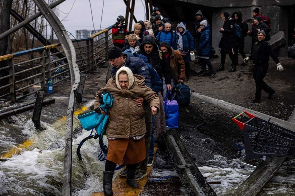  TOPSHOT - A man helps a woman evacuee cross a destroyed bridge as she and others flee the city of Irpin, northwest of Kyiv, on March 7, 2022. Ukraine dismissed Moscow's offer to set up humanitarian corridors from several bombarded cities on March 7, 2022, after it emerged some routes would lead refugees into Russia or Belarus. The Russian proposal of safe passage from Kharkiv, Kyiv, Mariupol and Sumy had come after terrified Ukrainian civilians came under fire in previous ceasefire attempts. (Photo by Dimitar DILKOFF / AFP)

      