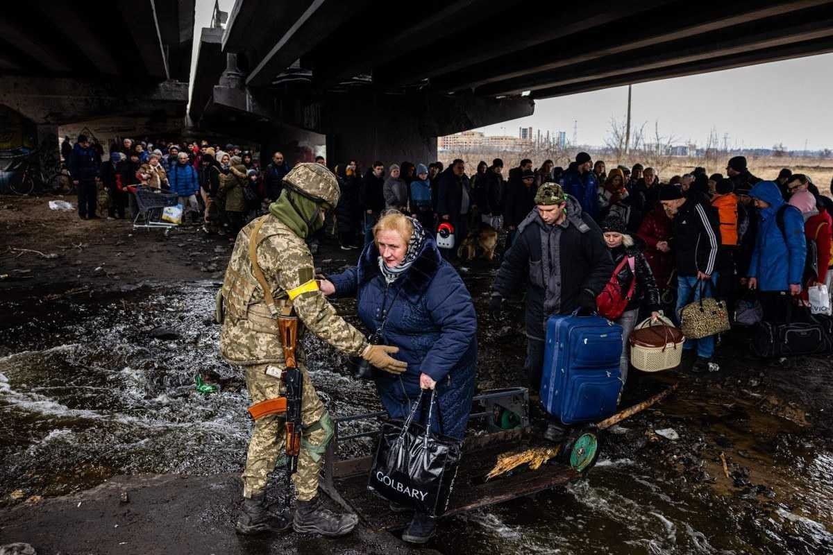 TOPSHOT - A Ukrainian serviceman helps evacuees gathered under a destroyed bridge, as they flee the city of Irpin, northwest of Kyiv, on March 7, 2022. Ukraine dismissed Moscow's offer to set up humanitarian corridors from several bombarded cities on March 7, 2022, after it emerged some routes would lead refugees into Russia or Belarus. The Russian proposal of safe passage from Kharkiv, Kyiv, Mariupol and Sumy had come after terrified Ukrainian civilians came under fire in previous ceasefire attempts. (Photo by Dimitar DILKOFF / AFP)

      