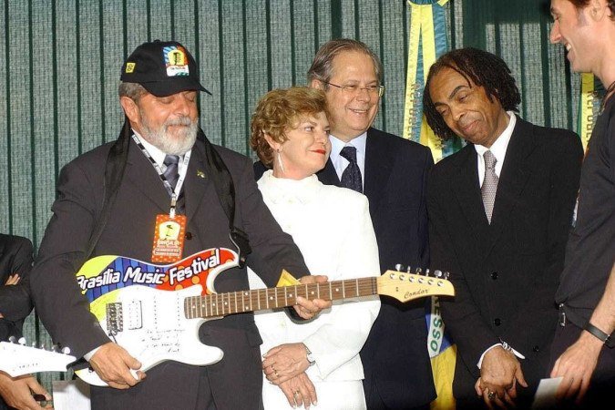  	Brasil. Brasilia - DF. Pauta: BMF Brasilia, 10/09/2003. Foto: Sergio Amaral/CB. Brasilia Music Festival (BMF). Presidente Luiz Inacio Lula da Silva toca guitarra que ganhou de Dinho Ouro Preto, vocalista da banda Capital Inicial (d), para ser leiloada em prol do programa Fome Zero. O ato serve para divulgar o BMF. Com o presidente, Marisa Leticia Lula da Silva, o ministro-chefe da Casa Civil Jose Dirceu e o ministro da Cultura, Gilberto Gil. 
      Caption 