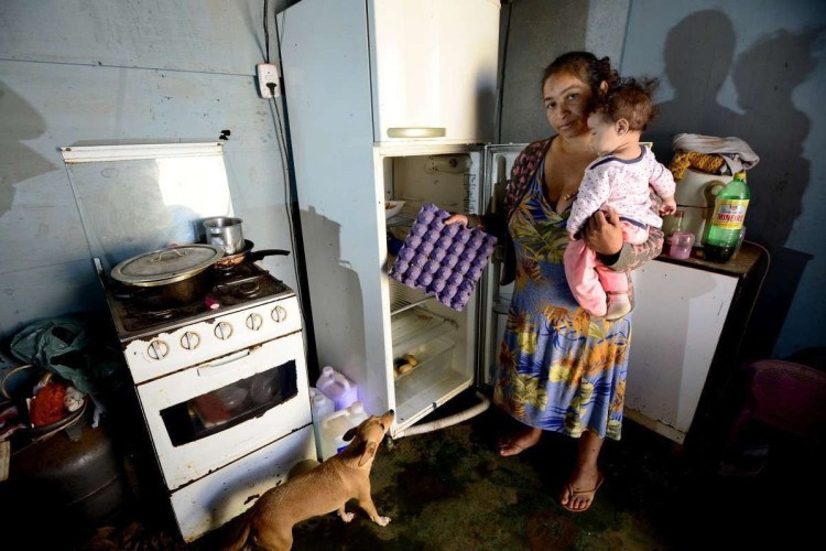Com o filho no colo, a moradora da Estrutural Maria Ribeiro mostra a geladeira vazia: "Hoje não tem nada para comer"