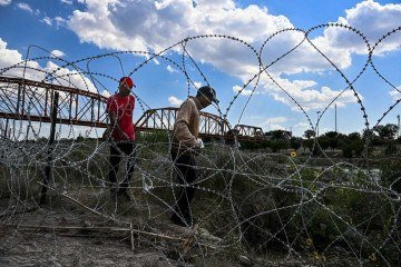 Imigrantes que cruzaram o Rio Grande caminham por cerca de arame farpado em Eagle , no Texas  -  (crédito: Chandan Khanna/AFP)