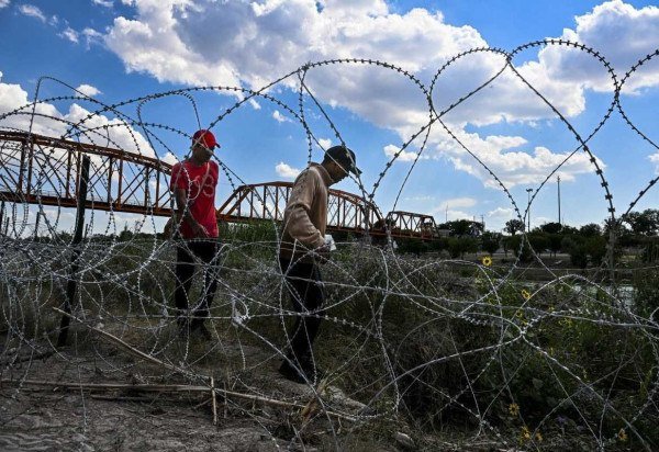 Imigrantes que cruzaram o Rio Grande caminham por cerca de arame farpado em Eagle Pass, no Texas  -  (crédito: Chandan Khanna/AFP)