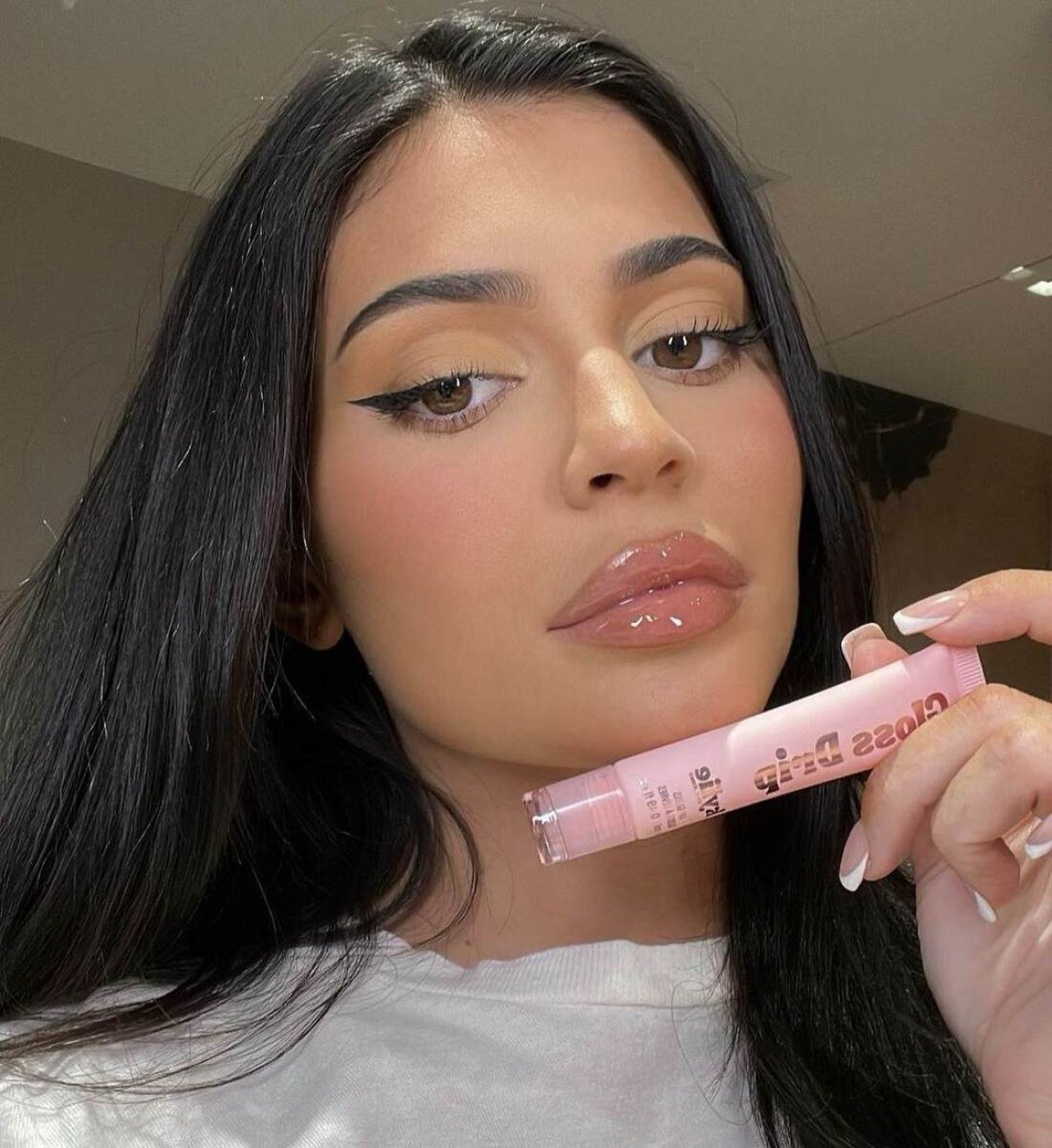 A influencer Kylie Jenner com as sobrancelhas mais finas, os cabelos lisos, compridos e divididos ao meio e com gloss noa lábios