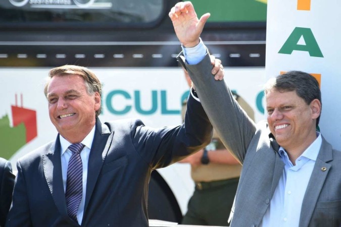 O presidente Jair Bolsonaro, em seu aniversário de 67 anos, ergue o braço do ministro da Infraestrutura Tarcísio de Freitas -  (crédito: EVARISTO SA / AFP)