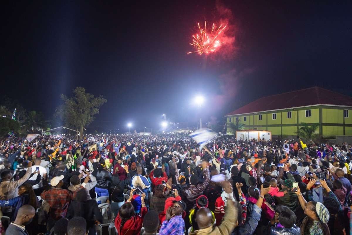 Fogos de artifício iluminam o céu enquanto as pessoas reagem enquanto comemoram após a contagem regressiva para o ano novo na Catedral Miracle Center em Kampala, Uganda