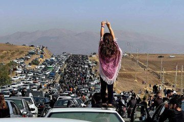 Uma mulher sem véu, em pé sobre o carro, enquanto milhares caminham até o enterro de Amini, em 2022  -  (crédito: UGC / AFP)