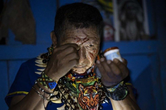 Isidro Lucitante, a healer of the indigenous Cofan ethnic group, paints his face with Achiote (Bixa orellana shrub) before the start of a Yage (Ayahuasca) drinking ceremony in Avie village, in Lago Agrio, Sucumbíos Province, Amazon region, Ecuador, on January 14, 2023. - This small community is famous for having driven mining companies out of their Amazonian territory in northern Ecuador. But the Cofán Avie natives have another mysterious and fascinating characteristic: they are the masters of ayahuasca, a hallucinogenic, medicinal plant and gateway "to the world of spirits." Also known as yagé, the ayahuasca is a decoction traditionally prepared by the peoples of the western Amazon basin, including the Siekopai in Peru, from the "Banisteriopsis caapi" liana. (Photo by Pedro PARDO / AFP) - (crédito: Pedro PARDO / AFP) Isidro Lucitante, a healer of the indigenous Cofan ethnic group, paints his face with Achiote (Bixa orellana shrub) before the start of a Yage (Ayahuasca) drinking ceremony in Avie village, in Lago Agrio, Sucumbíos Province, Amazon region, Ecuador, on January 14, 2023. - This small community is famous for having driven mining companies out of their Amazonian territory in northern Ecuador. But the Cofán Avie natives have another mysterious and fascinating characteristic: they are the masters of ayahuasca, a hallucinogenic, medicinal plant and gateway "to the world of spirits." Also known as yagé, the ayahuasca is a decoction traditionally prepared by the peoples of the western Amazon basin, including the Siekopai in Peru, from the "Banisteriopsis caapi" liana. (Photo by Pedro PARDO / AFP) - (crédito: Pedro PARDO / AFP)