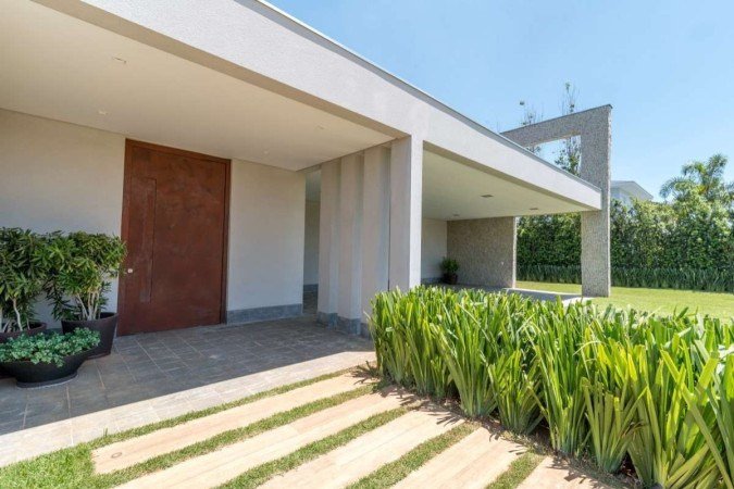 Nessa casa, a fachada tem ares mais elegantes.
O foco é nos revestimentos, nas texturas e na divisória para a garagem. Como decoração, os vasos de planta trazem um pouco do verde