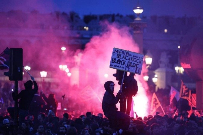 Manifestante sobre semáforo  segura placa com palavras de ordem contra Macron, em Place de la Concorde, em Paris 