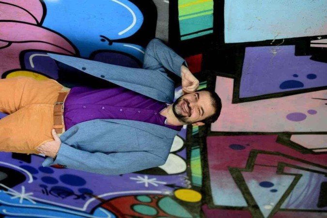 Henrique Santana, consultor em desenvolvimento organizacional  e lideranças, com tons de roxo, azul e laranja em suas roupas. 